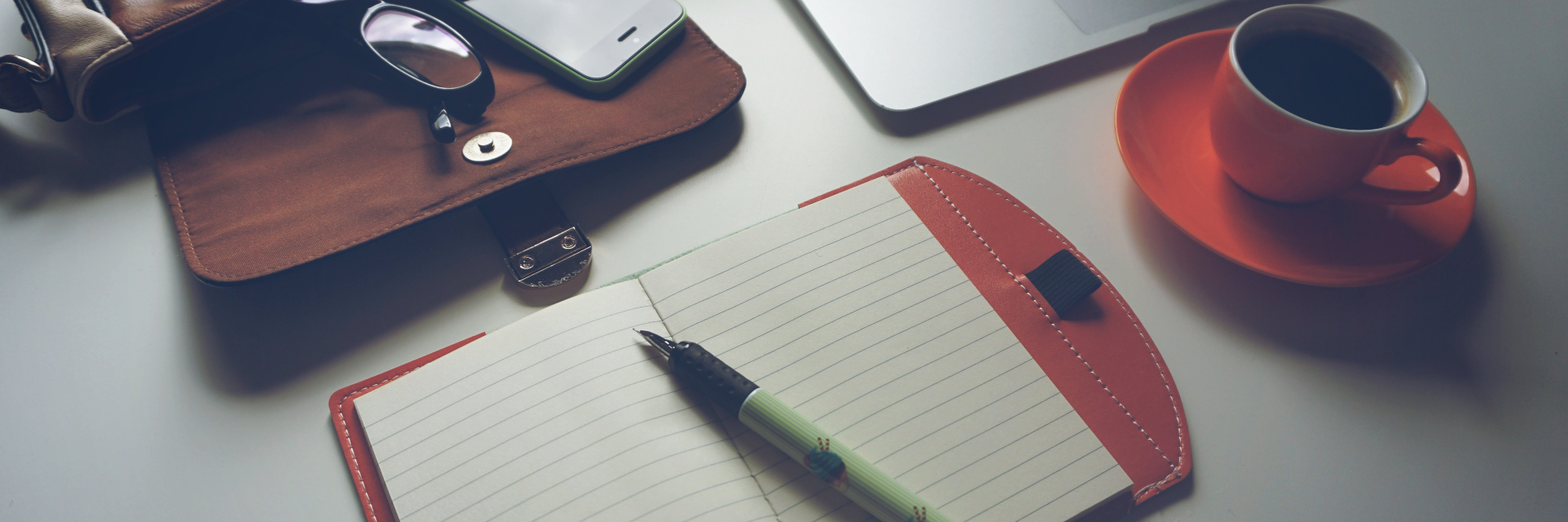 A desk with a computer, a bag, a notepad and coffee cup is featured.