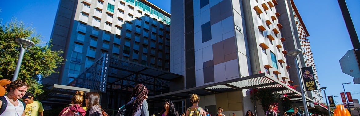 A downtown several story dormitory is the background as people bustle by